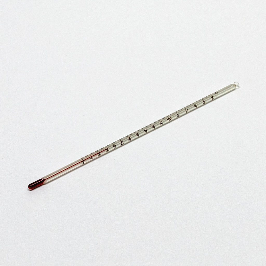 Das Bild zeigt ein Thermometer aus Glas mit einer roten Flüssigkeit, das zur Messung von Temperaturen verwendet wird. Es ist auf einer weißen Oberfläche platziert und besitzt eine Skala von 0 bis 100 Grad Celsius.