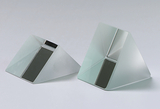 Das Bild zeigt zwei prismatische Glasskörper mit einer matten Oberfläche und einer horizontalen, schwarzen Fläche. Diese geometrischen Objekte werden häufig für physikalische Experimente verwendet, um Lichtbrechung und Reflexion zu demonstrieren.