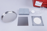 Das Bild zeigt verschiedene Experimentiermaterialien, darunter eine Aluminiumplatte, einen kleinen Glasbecher, eine Kerze und eine Metallschale, die für den Unterricht in Elementarphysik genutzt werden können. Diese Materialien sind in einer roten Box von Cornelsen angeordnet, die für Bildungszwecke gedacht ist.