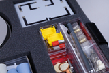Das Bild zeigt eine geöffnete Box mit Experimentierbedarf, die verschiedene Komponenten für wissenschaftliche Versuche enthält. Zu sehen sind gelbe Bauteile, Werkzeuge und Materialien, die für den Einsatz im Bildungsbereich konzipiert sind.