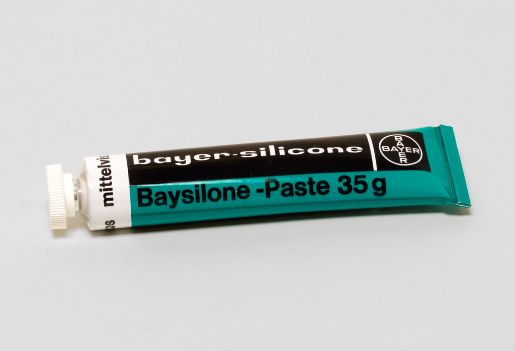 Das Bild zeigt eine Tube mit "Baysilone-Paste" der Marke Bayer, die ein Gewicht von 35 g hat. Die Tube ist in einem tealfarbenen Design mit schwarzem Schriftzug gestaltet und wird häufig für experimentelle Zwecke im Bildungswesen verwendet.