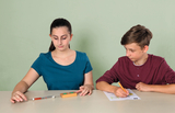 Auf dem Bild sind zwei Schüler an einem Tisch zu sehen. Die Schülerin verwendet ein Experimentiergerät, während der Schüler Notizen auf einem Arbeitsblatt macht.