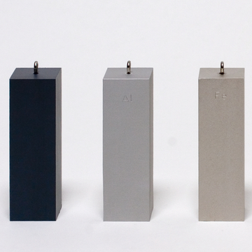 Das Bild zeigt drei rechteckige Blöcke aus unterschiedlichen Materialien, die in einem Experimentierbedarf-Shop angeboten werden. Die Blöcke sind beschriftet mit den chemischen Symbolen für Aluminium (Al) und Eisen (Fe) sowie einem dunklen Block, dessen Material nicht identifiziert ist.
