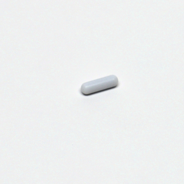 Das Bild zeigt eine kleine, weiße, längliche Pille oder Tablette, die auf einem weißen Hintergrund liegt. Sie scheint ein Experimentiermaterial zu sein, das möglicherweise in wissenschaftlichen oder educational Kontexten verwendet wird.