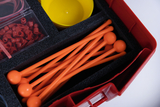 Das Bild zeigt einen roten Experimentierkasten, der eine Vielzahl von orangefarbenen Stäbchen mit runden Enden sowie ein paar gelben Schalen und rote Gummiteile enthält. Die Utensilien sind ordentlich in einem schaumstoffgepolsterten Innenraum angeordnet, ideal für Bildungszwecke.