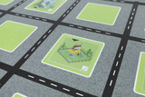 Auf der dargestellten Oberfläche sind verschiedene Quadrate abgebildet, die eine grüne Spiellandschaft mit einem kleinen Haus und verschiedenen Spielgeräten zeigen. Die bahnartige Struktur aus grauem Hintergrund und weißen Straßenlinien deutet auf ein geplantes Spiel- oder Lernkonzept hin.