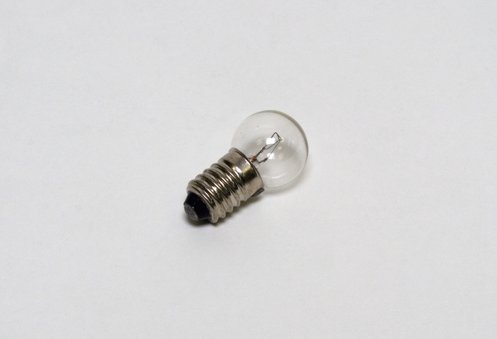 Eine kleine Glühbirne mit einem metallenen Sockel ist abgebildet. Sie hat eine durchsichtige Glaskuppel, in der sich der filigrane Glühdraht befindet.