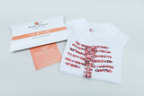 Ein weißes T-Shirt mit einem bunten, grafisch gestalteten Skelett-Motiv ist auf einem Tisch liegend zu sehen. Daneben befindet sich die Verpackung, die den Schriftzug "Body Planet" und den Slogan "A fun way to learn!" trägt.