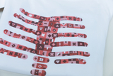Ein weißes T-Shirt zeigt ein auffälliges, grafisches Design in Form von Händen, die aus verschiedenen geometrischen Mustern bestehen. Die Farbpalette umfasst Rottöne und spielt mit Kontrasten, um ein modernes und ansprechendes Aussehen zu erzeugen.