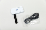 Ein weißes PASCO-Gerät zur drahtlosen Schallmessung liegt auf einer hellen Fläche. Daneben befindet sich ein in Plastik verpacktes, schwarzes USB-Kabel.