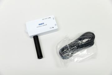 Ein weißes PASCO-Gerät zur drahtlosen Schallmessung liegt auf einer hellen Fläche. Daneben befindet sich ein in Plastik verpacktes, schwarzes USB-Kabel.