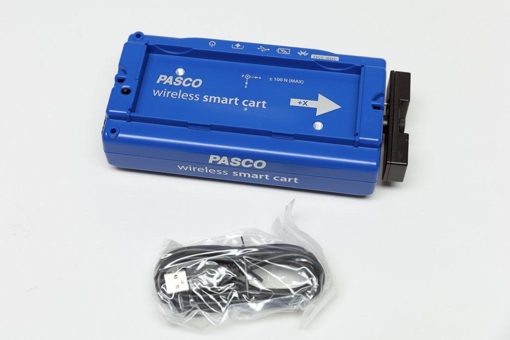 Ein blauer PASCO Wireless Smart Cart liegt auf einem weißen Hintergrund. Darunter befindet sich ein schwarzes USB-Kabel in einer durchsichtigen Kunststoffverpackung.