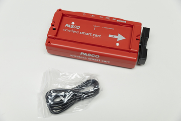 Ein roter PASCO Wireless Smart Cart liegt auf einer weißen Fläche. Daneben befindet sich ein schwarzes Kabel in einer transparenten Kunststoffverpackung.