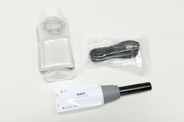 Ein drahtloser CO2-Sensor von PASCO liegt neben einer leeren Kunststoffflasche. Ein verpacktes USB-Ladekabel ergänzt das Set für wissenschaftliche Experimente.