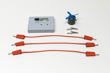 Ein Set aus einem kleinen Elektromotor mit blauem Propeller und drei roten Verbindungskabeln liegt bereit. Ergänzt wird das Kit durch eine graue Basisplatte sowie zwei Krokodilklemmen.