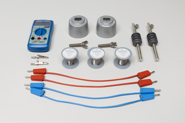 Ein blaues Digitalmultimeter, verschiedene Metallzylinder, Schrauben und Anschlusskabel liegen auf weißem Grund. Es handelt sich um ein physikalisches Experimentierset zur Bestimmung des elektrischen Widerstands.