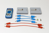 Ein blaues Digitalmultimeter liegt neben zwei grauen Prüfmodulen auf weißem Grund. Ergänzt wird das Set durch diverse rote und blaue Verbindungskabel sowie kleine Metallstifte.