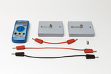 Ein blaues Digitalmultimeter liegt neben zwei grauen Messblöcken. Drei rote und schwarze Verbindungskabel sowie ein kleiner Metallstift ergänzen das Set.