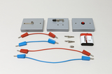 Ein physikalisches Experimentierset umfasst drei graue Module mit Schaltern sowie rote und blaue Anschlusskabel. Ergänzt wird das Set durch Krokodilklemmen und eine Batterie.
