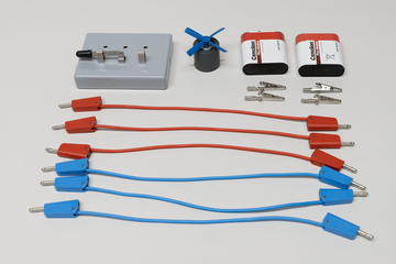 Ein Set für Physikexperimente enthält rote und blaue Anschlusskabel sowie Krokodilklemmen. Ergänzt wird das Kit durch zwei Batterien, einen kleinen Elektromotor mit Propeller und eine graue Basisstation.