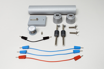 Ein physikalisches Experimentierset besteht aus einem Metallzylinder, verschiedenen Adaptern und Kontaktschuhen. Ergänzt wird das Set durch zwei blaue und ein rotes Verbindungskabel sowie zwei metallischen Stiften.