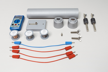 Ein physikalisches Experimentierset mit Multimeter, verschiedenen Metallzylindern und Anschlusskabeln ist auf weißem Grund angeordnet. Ergänzt wird das Set durch zwei Schieberegler sowie eine kleine Glühbirne.