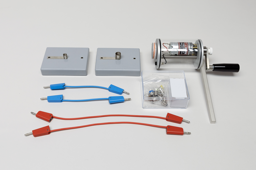 Ein Set für physikalische Experimente umfasst eine Handkurbel-Dynamo-Einheit sowie zwei Kontaktplatten. Ergänzt wird das Set durch rote und blaue Anschlusskabel sowie eine kleine Box mit Zubehör.
