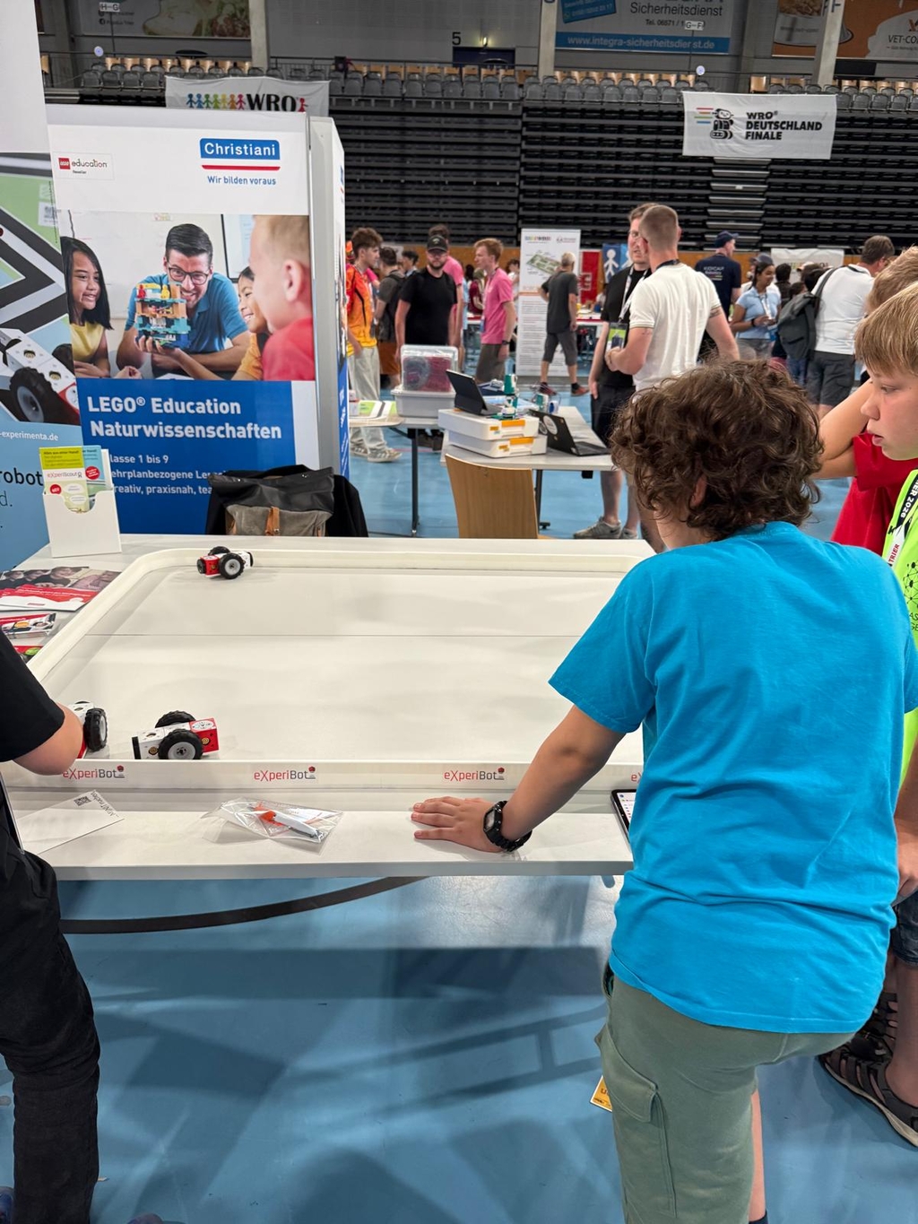 Ein Junge in einem blauen T-Shirt betrachtet an einem Stand ein Experiment mit kleinen Roboterautos. Ein Aufsteller wirbt daneben für Naturwissenschaften von LEGO Education.