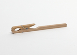 Eine hölzerne Wäscheklammer liegt horizontal auf einem weißen Hintergrund. Das schlichte Utensil besteht aus zwei Holzleisten und einer Metallfeder.