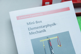 Ein Handbuch der Reihe „Cornelsen Experimenta“ liegt auf einer hellen Fläche. Es befasst sich mit Elementarphysik und Mechanik für eine Mini-Box.