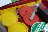 In einer roten Box befinden sich verschiedene Kunststoffscheiben in Gelb und Rot sowie ein Metallstab. Ergänzt wird das Set durch eine weiße Rolle mit der Aufschrift „Mason Cord“.