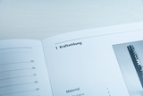 Ein aufgeschlagenes Lehrbuch zeigt das Kapitel „1 Kraftwirkung“. Links ist ein Inhaltsverzeichnis mit Seitenzahlen, rechts eine Materialliste sowie ein Teilausschnitt einer Abbildung zu sehen.