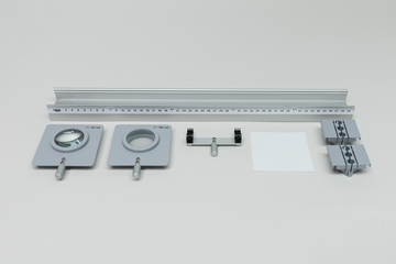 Ein Physik-Set zur Optik umfasst ein Lineal, zwei Linsenhalter mit unterschiedlichen Brennweiten und ein weißes Papier. Ergänzt wird das Set durch eine Halterung sowie weitere graue Kunststoffkomponenten.