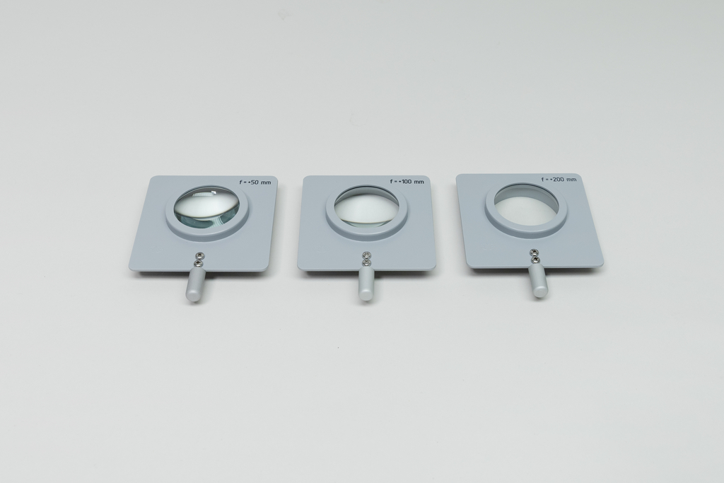 Drei optische Sammellinsen in grauen quadratischen Fassungen liegen nebeneinander. Die Linsen sind mit verschiedenen Brennweiten von 50 mm, 100 mm und 200 mm beschriftet.