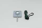 Eine Sammellinse mit einer Brennweite von 50 mm ist in einer grauen Halterung fixiert. Daneben liegt eine kleine, grüne Taschenlampe mit einem schwarzen Trageband.