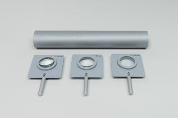Drei Sammellinsen mit unterschiedlichen Brennweiten (50 mm, 100 mm und 200 mm) liegen in grauen Halterungen vor. Darüber befindet sich eine graue, strukturierte Rolle.
