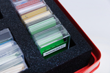 Mehrere kleine, transparente Kunststoffboxen mit farbigen Karten liegen in einer schwarzen Schaumstoffauslage. Eine Box ist mit „Kartensatz D1A 2.1“ beschriftet und befindet sich in einem roten Koffer.