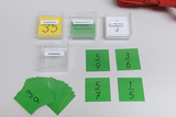 Vier durchsichtige Kunststoffboxen enthalten beschriftete Karten für den Mathematikunterricht. Auf dem Tisch liegen zudem mehrere grüne Karten mit verschiedenen Brüchen verteilt.