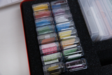 Ein roter Koffer enthält mehrere transparente Kunststoffboxen mit farbigen Papieren. Die Boxen sind ordentlich in einem schwarzen Schaumstoffeinleger sortiert.